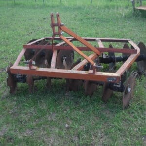 DSCF4521 - Montana Auctions by Kevin Hill Rusty orange disk harrow resting on green grass in a field.