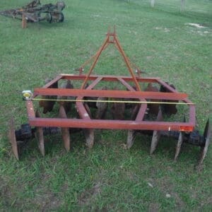 DSCF4524 - Montana Auctions by Kevin Hill Red metal disc harrow on a grassy field, used for tilling soil with multiple concave steel discs.