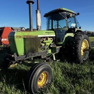 IMG_1295 - Montana Auctions by Kevin Hill Front-left view of a weathered green John Deere tractor in a grassy field under a clear blue sky.
