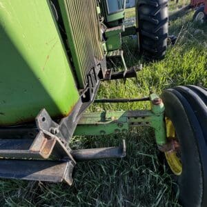 IMG_1297 - Montana Auctions by Kevin Hill Close-up of a green tractor's front end, showing a rusted hitch, metal steps, and large front tire on grass.