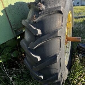 IMG_1298 - Montana Auctions by Kevin Hill Close-up of a large tractor rear tire with deep V-tread, mounted on a green agricultural vehicle in a grassy field.