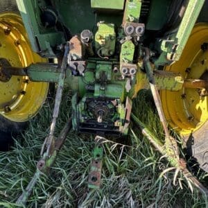 IMG_1301 - Montana Auctions by Kevin Hill Rear view of a green tractor showing a worn three-point hitch and yellow wheels in tall grass around the arms and linkage.