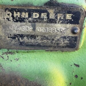 IMG_1302 - Montana Auctions by Kevin Hill Dirty metal nameplate on a green John Deere machine showing the brand name and serial numbers (made in USA). Arrow: 4430P 023885R. Weathered and dusty surface around the plate.