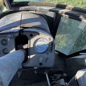 IMG_1306 - Montana Auctions by Kevin Hill Interior view of a dusty tractor cab: round speedometer gauge, steering column, pedals, and gloves on the rubber floor mats, with a green field outside the window