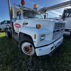 IMG_1310 - Montana Auctions by Kevin Hill Front-right view of a weathered white utility tow truck with amber lights in a grassy lot under a blue sky.