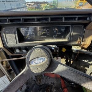 IMG_1315 - Montana Auctions by Kevin Hill Old Ford truck interior with a dusty four-spoke steering wheel and faded dashboard gauges seen through the windshield outside in a yard.