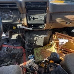 IMG_1316 - Montana Auctions by Kevin Hill Dirty truck cab interior with a manual gear shifter, dusty dashboard, and tangled wires on the floor.