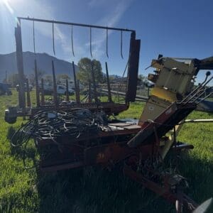 IMG_1319 - Montana Auctions by Kevin Hill Red farm rake/baler on a trailer with tangled hoses, parked in a sunlit grassy field.