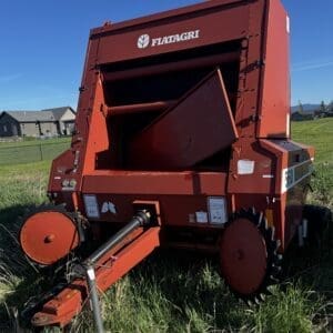 IMG_1322 - Montana Auctions by Kevin Hill Red Fiatagri hay baler parked in tall grass on a sunny rural field with a blue sky above.