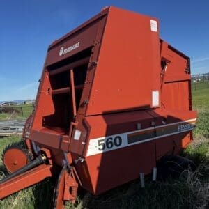 IMG_1323 - Montana Auctions by Kevin Hill Red Hesston 560 hay baler parked in a grassy field with a clear blue sky overhead.