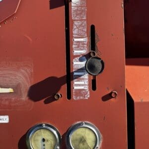 IMG_1324 - Montana Auctions by Kevin Hill Red industrial control panel with a vertical gauge slot, a black knob, and two round dials at the bottom under a weathered label strip.