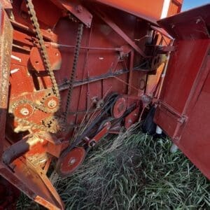 IMG_1328 - Montana Auctions by Kevin Hill Close-up of red farming equipment with gears, chains, and belts resting on tall grass.