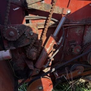 IMG_1335 - Montana Auctions by Kevin Hill Rusty agricultural machinery with chains, gears, and a hydraulic cylinder on a red frame.