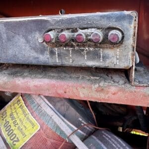 IMG_1338 - Montana Auctions by Kevin Hill Dusty, weathered control panel with five red push buttons mounted on a red machine, with dirty cobwebs and faded labels underneath each button.