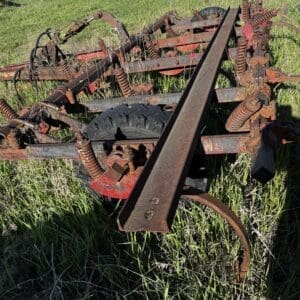IMG_1341 - Montana Auctions by Kevin Hill Rusty agricultural cultivator frame with coil springs and a single wheel, abandoned in tall grass in a field.
