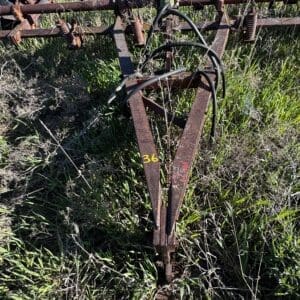 IMG_1343 - Montana Auctions by Kevin Hill Close-up of a rusted farm implement hitch with black hoses, in tall grass; the frame is marked with yellow '36'.