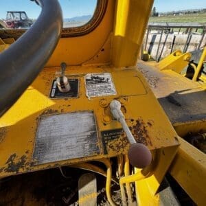 IMG_1353 - Montana Auctions by Kevin Hill Control panel of a dusty yellow construction machine with levers and warning labels, viewed from the operator's seat near a window.