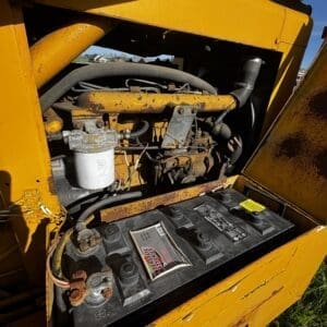 IMG_1354 - Montana Auctions by Kevin Hill Open engine compartment of a yellow industrial machine showing a diesel engine and battery inside. outdoor scene in a field.