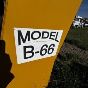 IMG_1355 - Montana Auctions by Kevin Hill Yellow industrial equipment with a white label reading 'MODEL B-66' in a sunny field; trucks visible in the background.