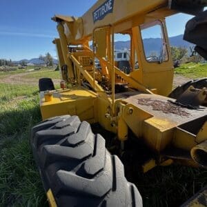 IMG_1358 - Montana Auctions by Kevin Hill Yellow Pettibone construction crane in a grassy field, with large treaded tires and a clear blue sky; mountains visible in the background.