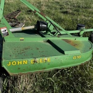IMG_1359 - Montana Auctions by Kevin Hill Green John Deere 616 mower attachment in a grassy field, rust spots visible, with red farm equipment and houses in the background.