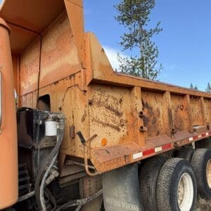 IMG_6526 - Montana Auctions by Kevin Hill Rusty orange dump trailer with dirt-streaked sides, exposed hydraulics, and dual rear tires labeled Western Trailers.
