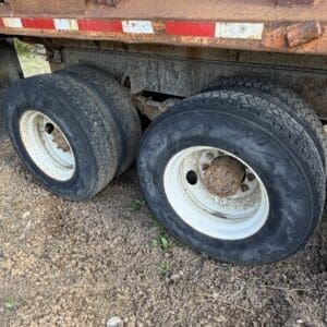 IMG_6528 - Montana Auctions by Kevin Hill Rusty orange dump trailer with two rear wheels on a dirt ground, showing corroded rims and worn tires.