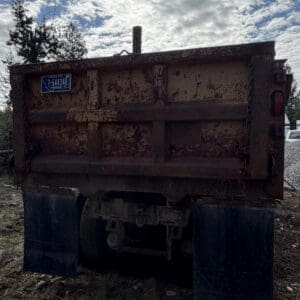 IMG_6530 - Montana Auctions by Kevin Hill Back of a rusty dump truck with a Montana license plate, sitting in a dirt lot under a cloudy sky.