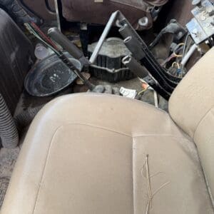 IMG_6534 - Montana Auctions by Kevin Hill Messy car interior with exposed wires, metal brackets, and a brown leather seat, plus dust and debris on the floor and seat edge.