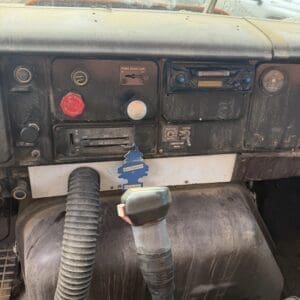 IMG_6536 - Montana Auctions by Kevin Hill Dusty truck dashboard with worn panels, red emergency knob, gauges, and exposed hoses; outside yard visible through the windshield.