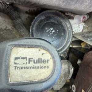 IMG_6537 - Montana Auctions by Kevin Hill Close-up of a dusty engine bay component with a round cap labeled 'Fuller Transmissions' on the transmission housing.