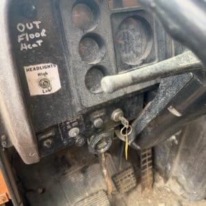 IMG_6538 - Montana Auctions by Kevin Hill Dusty vehicle dashboard with gauges, a headlight switch, ignition keys, and three pedals on a dirty floor.