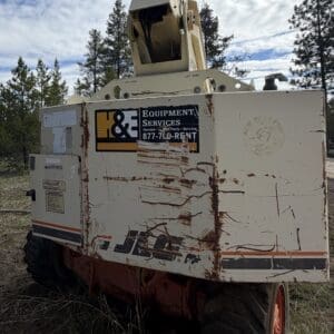 IMG_6547 - Montana Auctions by Kevin Hill White mobile elevated work platform with a raised bucket, parked in a pine forest; side panel reads Equipment Services Rentals/Parts/Service (sign is weathered).