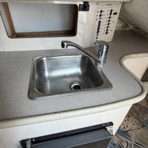 IMG_6561 - Montana Auctions by Kevin Hill Compact kitchenette with stainless sink, curved faucet, and countertop; control panel to the right and an open cabinet below.