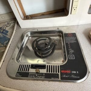 IMG_6563 - Montana Auctions by Kevin Hill Dusty vintage single-burner electric stovetop with coil burner in a worn kitchen counter, cabinet opening above, and dual outlets nearby.