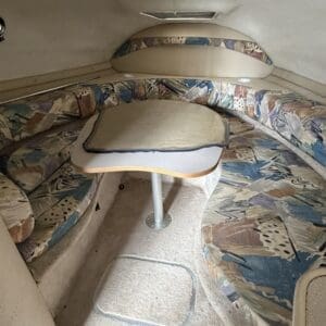 IMG_6564 - Montana Auctions by Kevin Hill Interior of a small boat cabin with curved cushioned seating around a central table on a pedestal; patterned upholstery in beige, blue, and brown tones