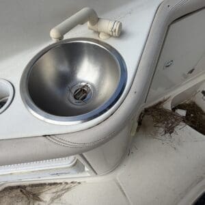 IMG_6566 - Montana Auctions by Kevin Hill Round stainless sink set into a boat console with a beige curved faucet, surrounded by dust and pine needles on the deck.