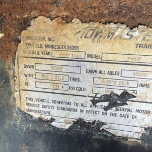 IMG_6569 - Montana Auctions by Kevin Hill Close-up of a weathered vehicle data plate peeling from a rusty surface, showing fields for weight, tires, and model (partially legible).