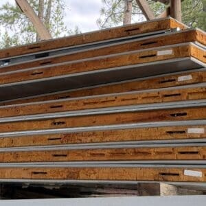 IMG_6576 - Montana Auctions by Kevin Hill Stacked construction panels: orange-brown OSB/plywood with metal edging, outdoors among trees.
