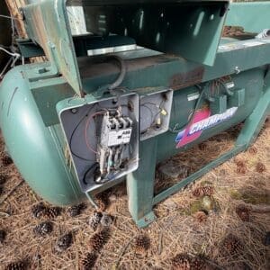 IMG_6585 - Montana Auctions by Kevin Hill Green industrial machine outdoors with an open electrical control panel showing wires and a contactor; rust and pinecones on the ground nearby.