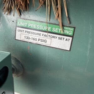 IMG_6587 - Montana Auctions by Kevin Hill Green industrial machine with a label reading 'Unit pressure factory set at 130-165 PSIG'; dried plant fibers rest on top.