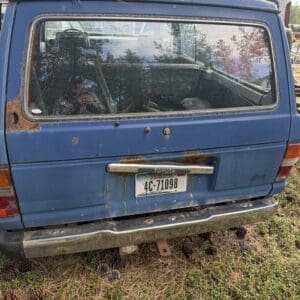 IMG_6593 - Montana Auctions by Kevin Hill Rusted blue Toyota SUV rear view with a dirty window reflecting the photographer, sitting on a grassy, cone-strewn lot; license plate 4C-71098.