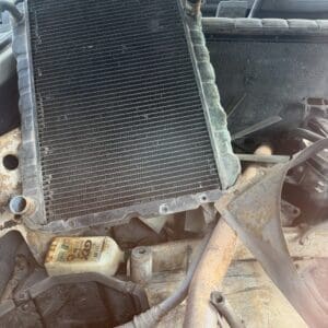 IMG_6594 - Montana Auctions by Kevin Hill Detached radiator resting in a rusty car engine bay, coolant bottle nearby and exposed hoses visible in a dusty vehicle interior