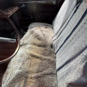 IMG_6604 - Montana Auctions by Kevin Hill Interior of an old car with a shaggy beige seat cover over the driver’s seat and a striped blanket on the passenger seat.