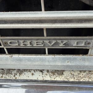 IMG_6608 - Montana Auctions by Kevin Hill Close-up of a weathered Chevrolet grille with a rusted chrome emblem, showing dirt and age.