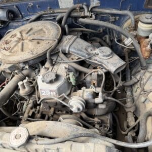 IMG_6613 - Montana Auctions by Kevin Hill Dusty engine bay featuring a 22R inline engine with a round air cleaner and numerous hoses and wires visible under the hood.