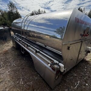 IMG_6617 - Montana Auctions by Kevin Hill Shiny stainless steel water tanker trailer labeled 'FOR DRINKING WATER' parked on dirt with pipes along its side.
