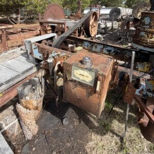 IMG_6620 - Montana Auctions by Kevin Hill Rusty industrial control box and belt-driven machinery in a weathered outdoor scrap yard setting with overgrown grass.
