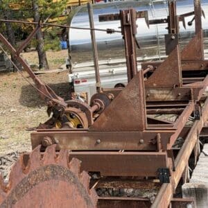 IMG_6621 - Montana Auctions by Kevin Hill Rusty, abandoned piece of vintage farm machinery with a large circular cutting gear on a trailer-like frame, outdoors.