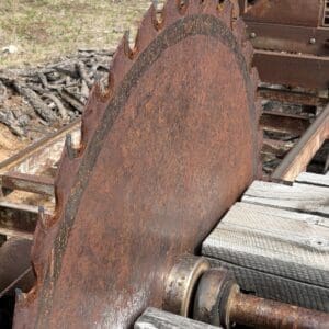 IMG_6622 - Montana Auctions by Kevin Hill Large rusty circular saw blade with jagged teeth mounted on a weathered machine beside wooden planks.